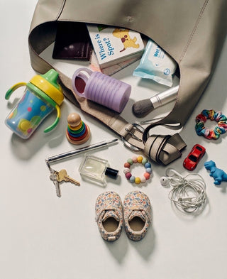 A mom's tote bag spilled open with a sippy cup, board book, wet wipes, keys, baby shoes and a Subtl Beauty Stak