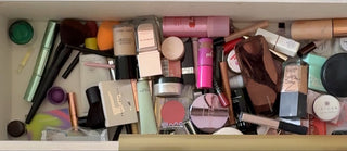 Open drawer filled with various makeup items, with a hand reaching in.
